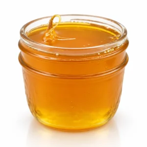Honey oil in a clear ridged glass jar, thick golden amber oil on a white background